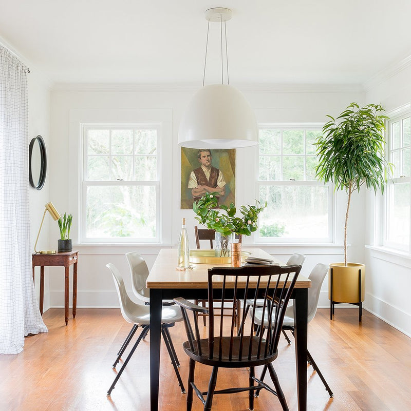 Ostara pendant hanging over a wood dining table in a bright white dining room with mixed chairs and potted plants