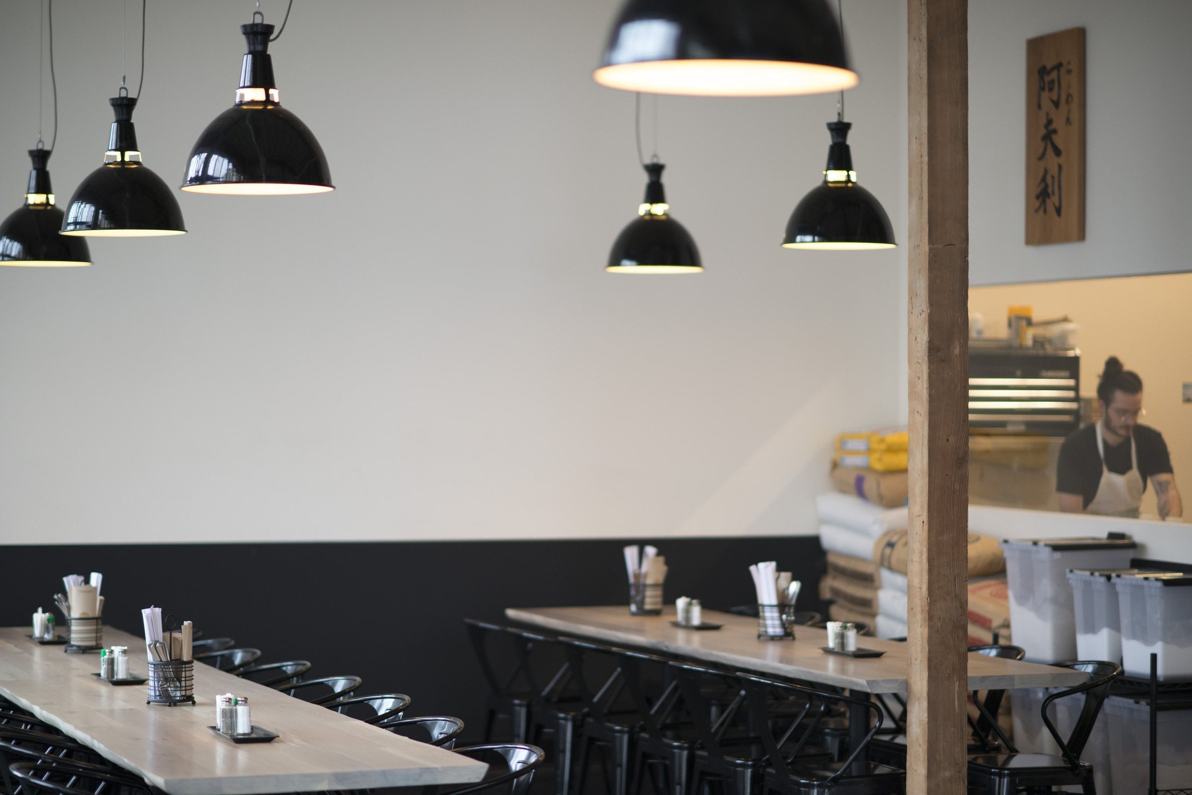 Communal wooden tables and black pendant lights in Afuri Ramen interior with a chef working behind the counter