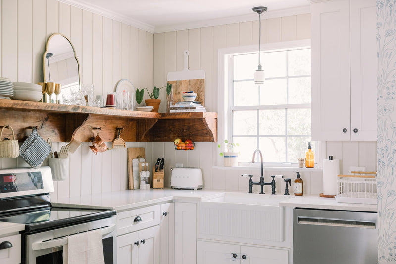 A light-filled kitchen with wallpaper and a pendant over the sink. 