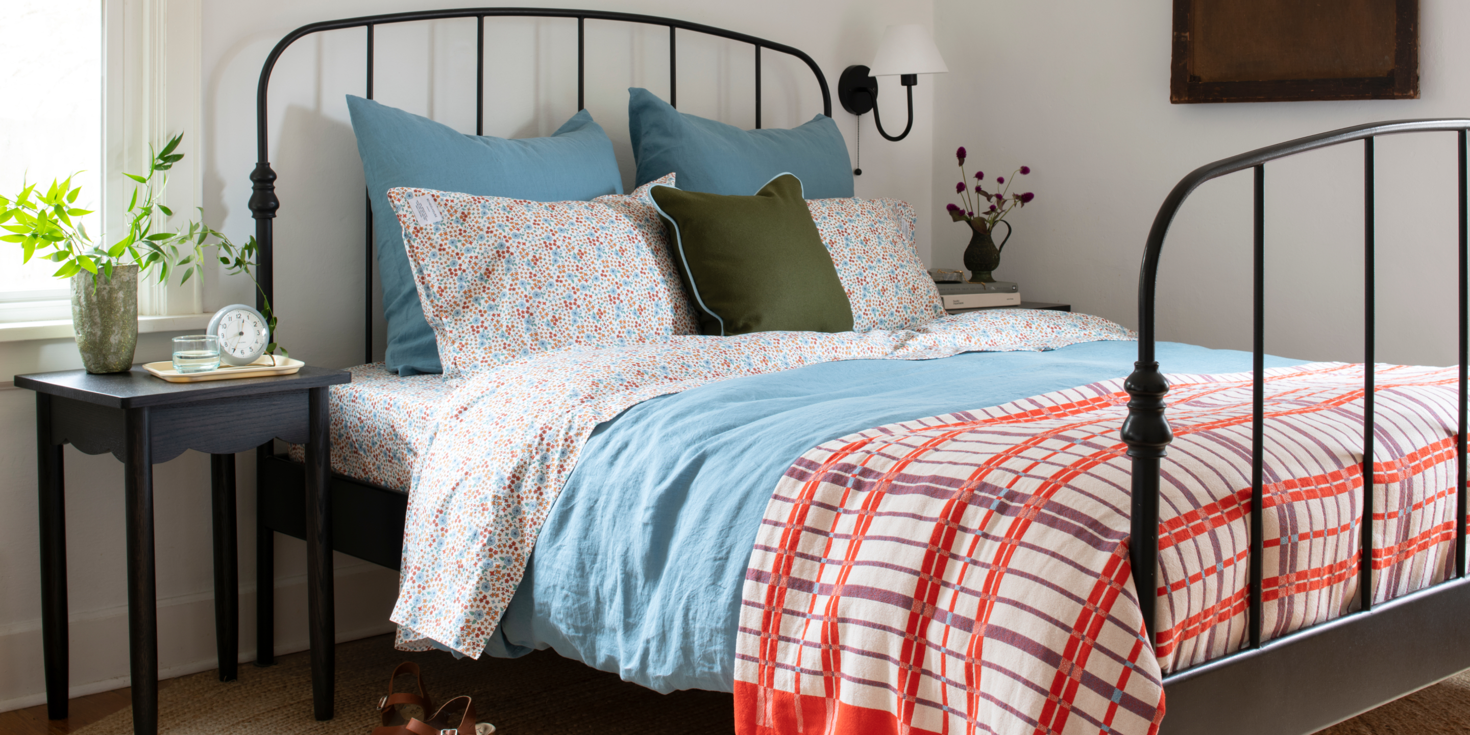 Rod iron bed with blue bedding and red accents in a white bedroom 